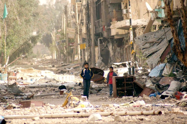 Boys walk along a damaged street filled with debris in Deir al-Zor